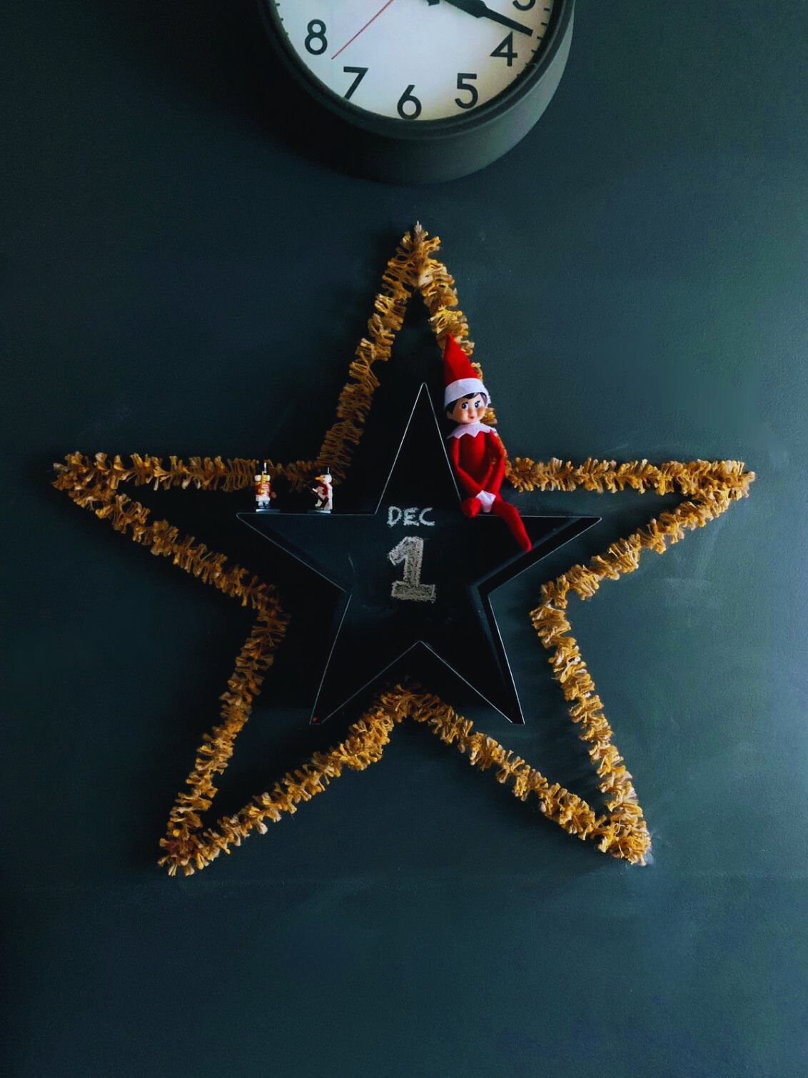 Bright gold Strinsel string tinsel forming a star on a dark wall with an elf_on_the_shelf 
