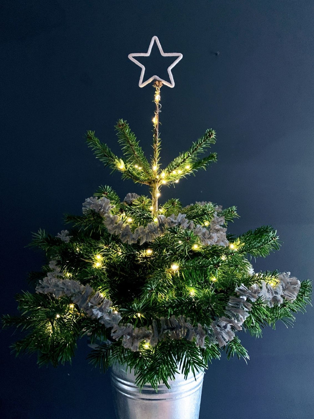 Small Christmas tree topped with a star  and draped in silvery pewter Strinsel jute string tinsel on a dark background