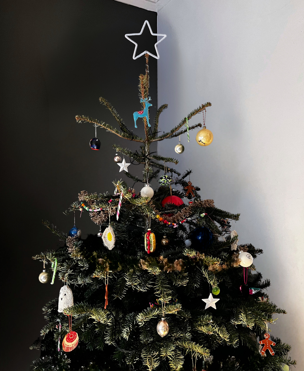 Star topped decorated Christmas tree with various ornaments against a dark wall.