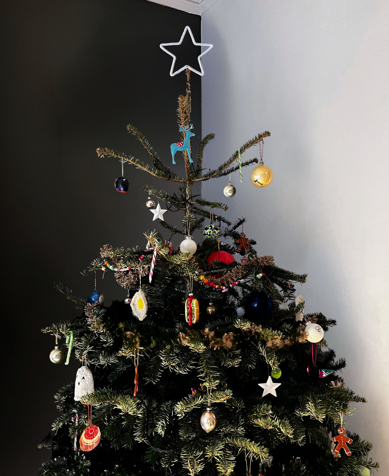 Star topped decorated Christmas tree with various ornaments against a dark wall.