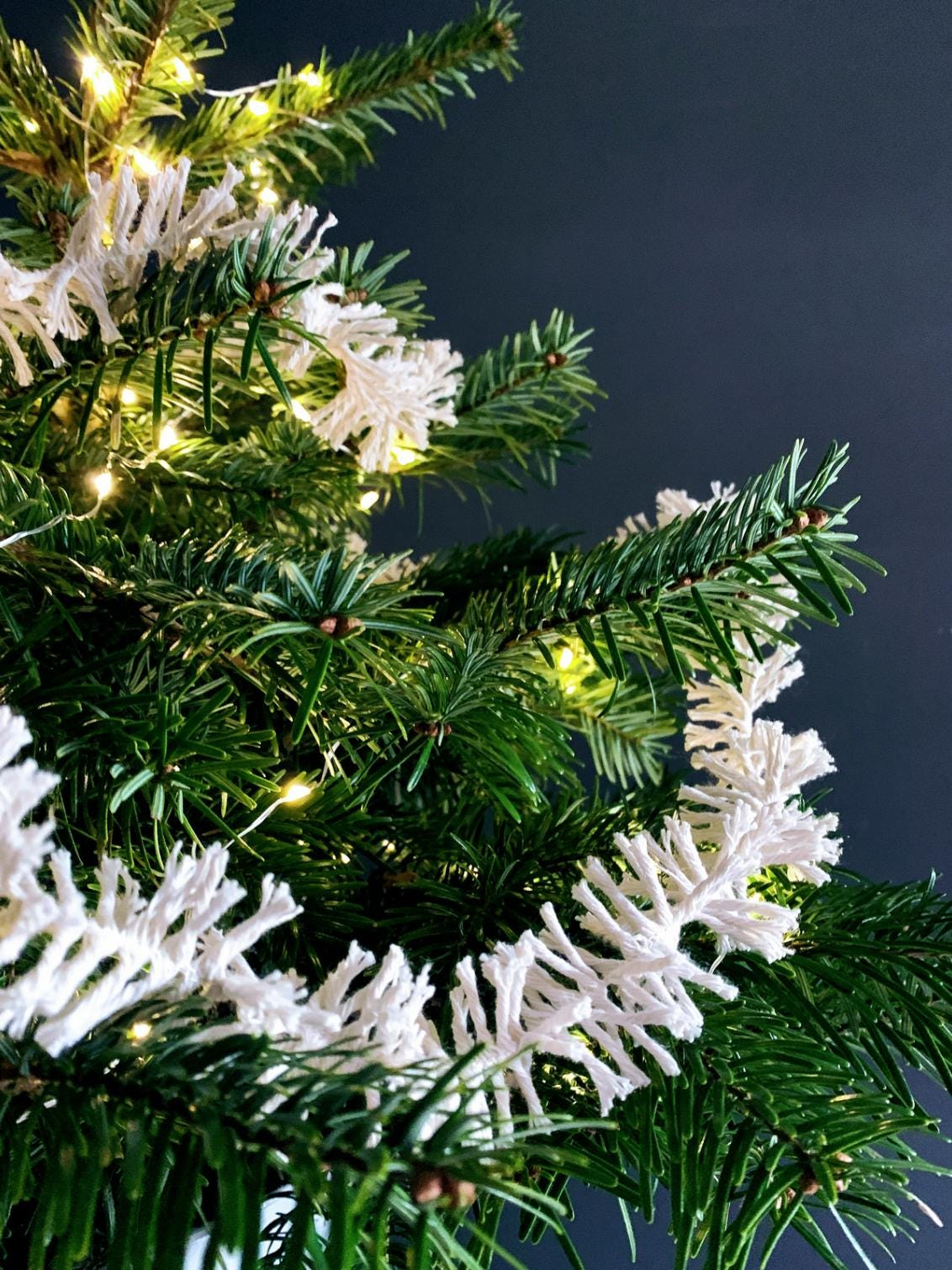 Close-up of a decorated Christmas tree with lights and white Strinsel string tinsel against a dark background