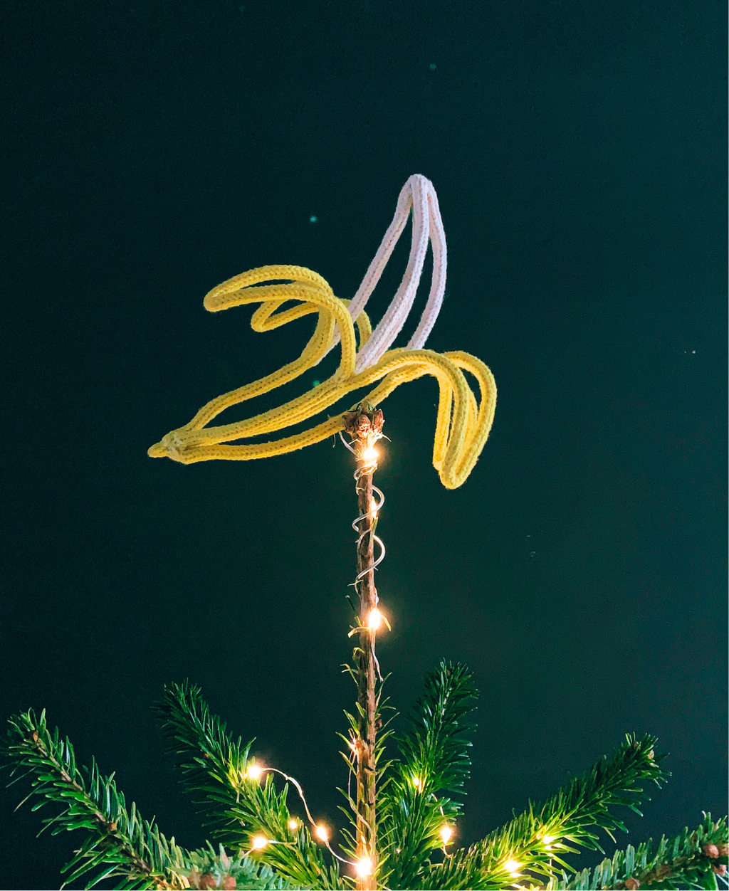 Christmas tree topped with a French knitted string and wire sculpted banana against a dark background