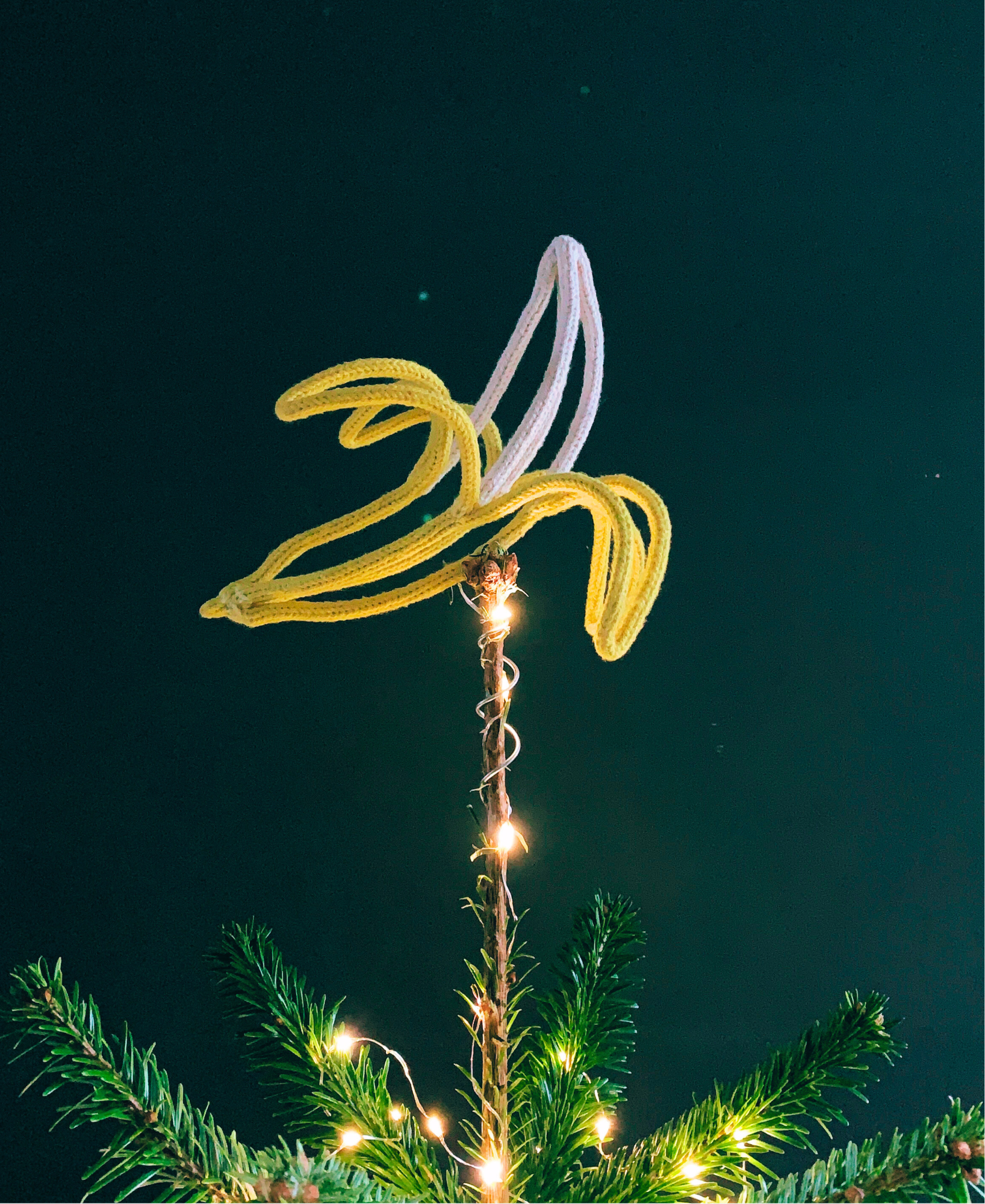 Christmas tree topped with a French knitted string and wire sculpted banana against a dark background