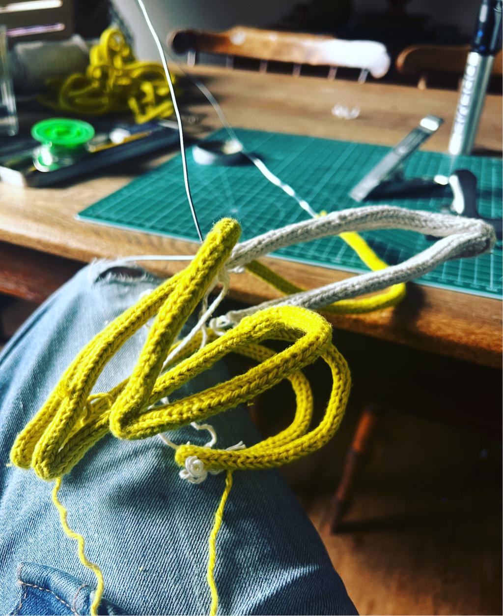 French knitted string and wire sculpted banana work in progress against a wooden table and green cutting mat