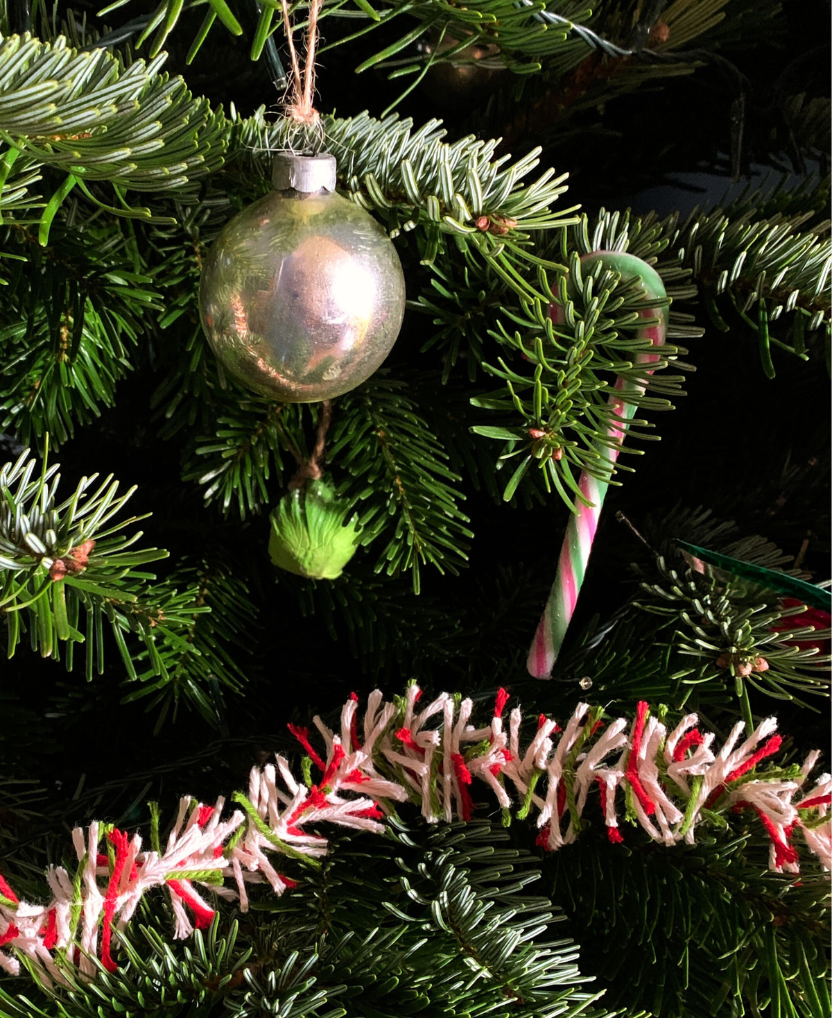 Real Christmas tree branches decorated with a silver bauble, a candy cane and draped in red, white and green jute Strinsel string tinsel