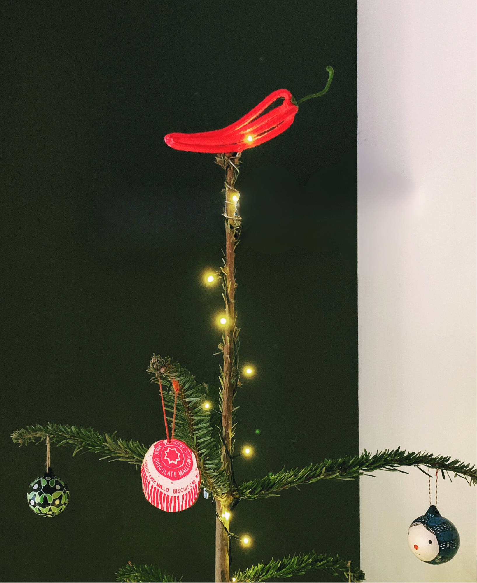 Decorative Christmas tree topped with a French knitted and wire sculpted red chilli against a dark background.