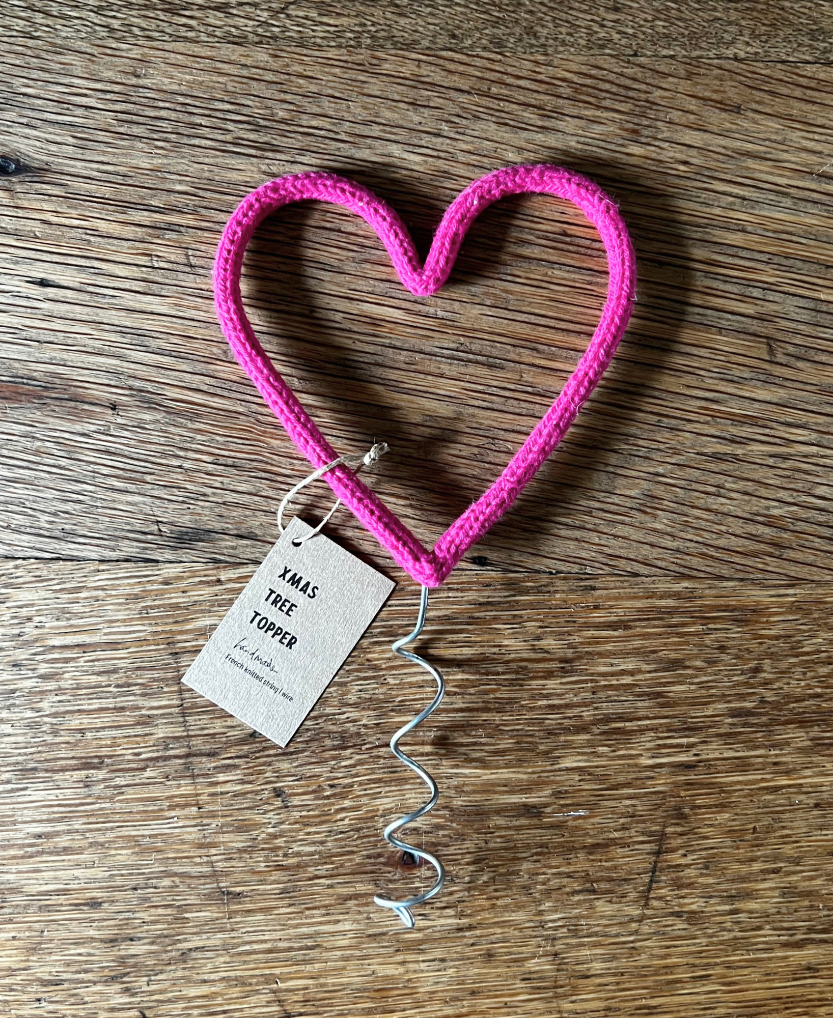 Pink heart-shaped tree topper with a tag on a wooden surface