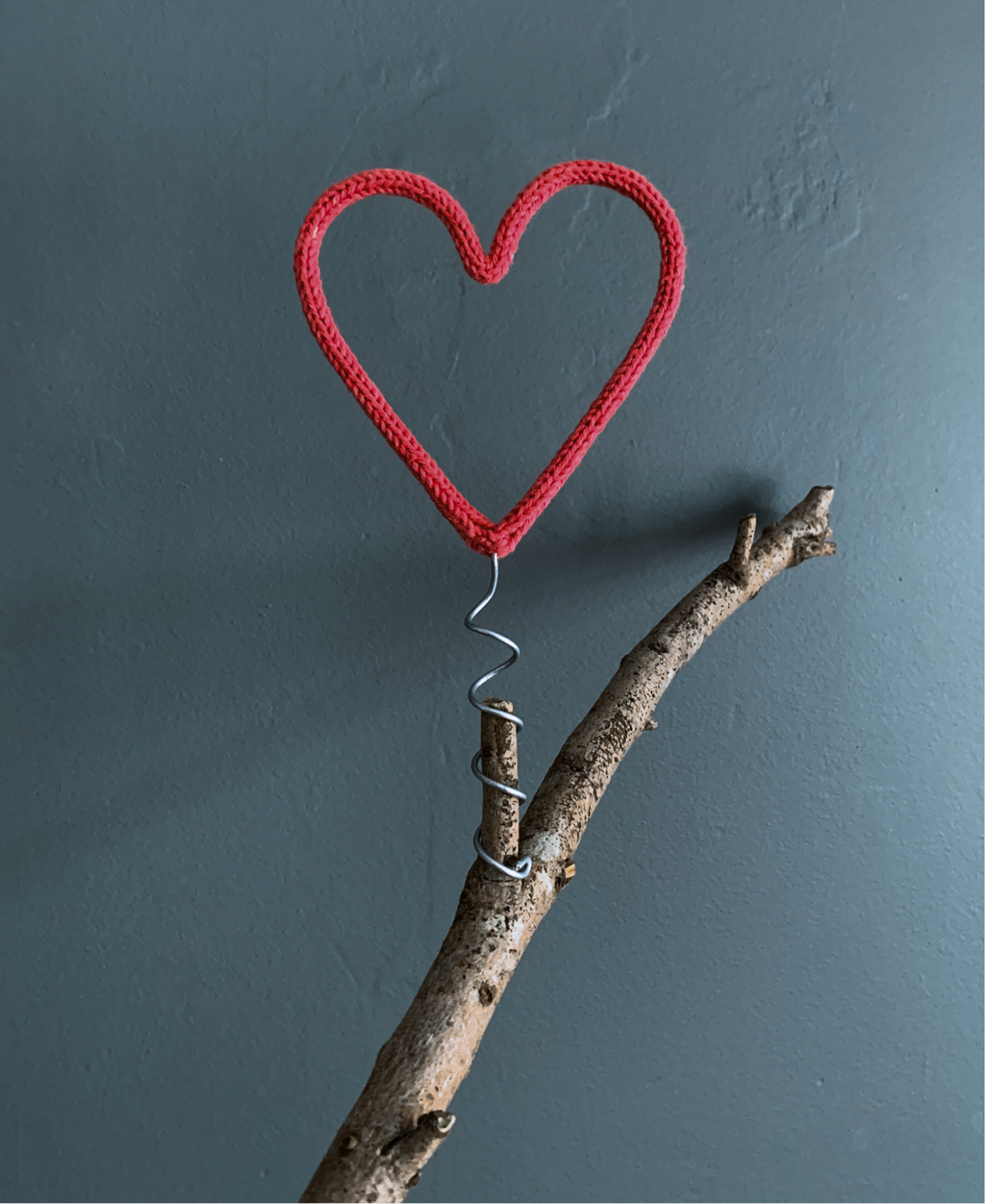 Red heart-shaped tree topper attached to a branch against a grey background