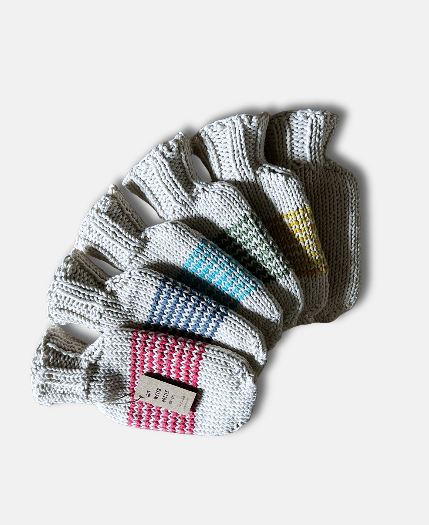 Set of six pairs of mini hot water bottles with different colour stripes on a light grey background