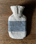 Knitted hot water bottle cover with blue stripes on a wooden surface
