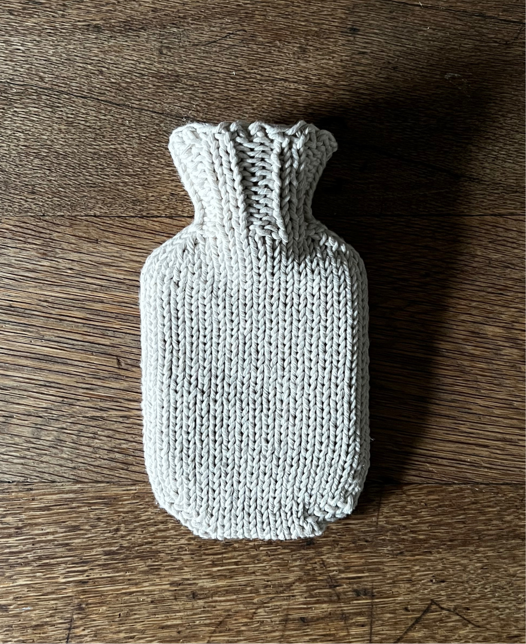 Knitted cotton string mini hot water bottle cover on a wooden surface
