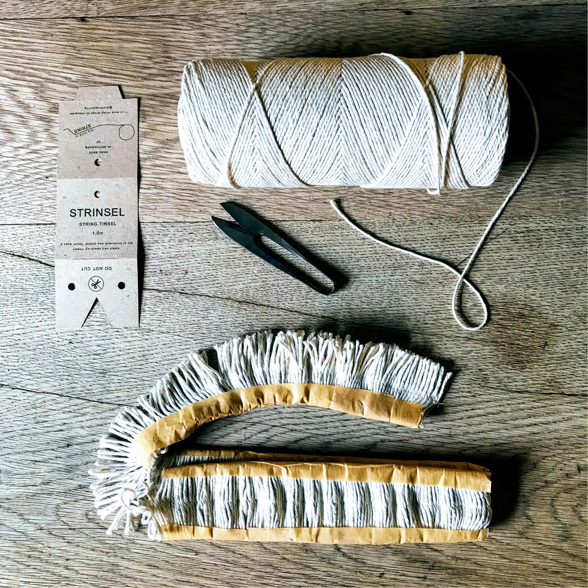 Spool of  cotton string, Strinsel string tinsel label, scissors, and part made garland on a wooden table top
