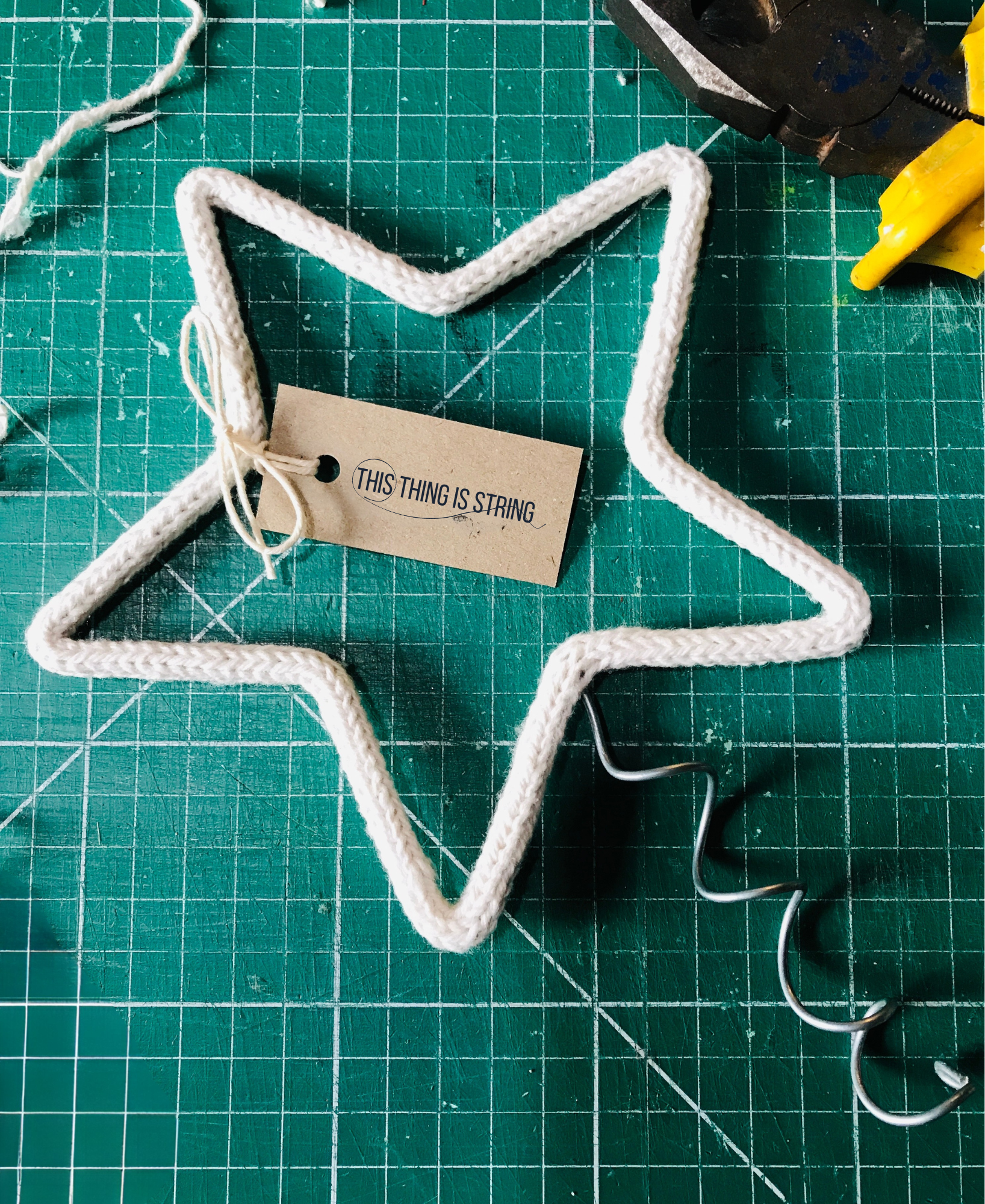 French knitted string and wire sculpted star tree topper on a green cutting mat with hand tools