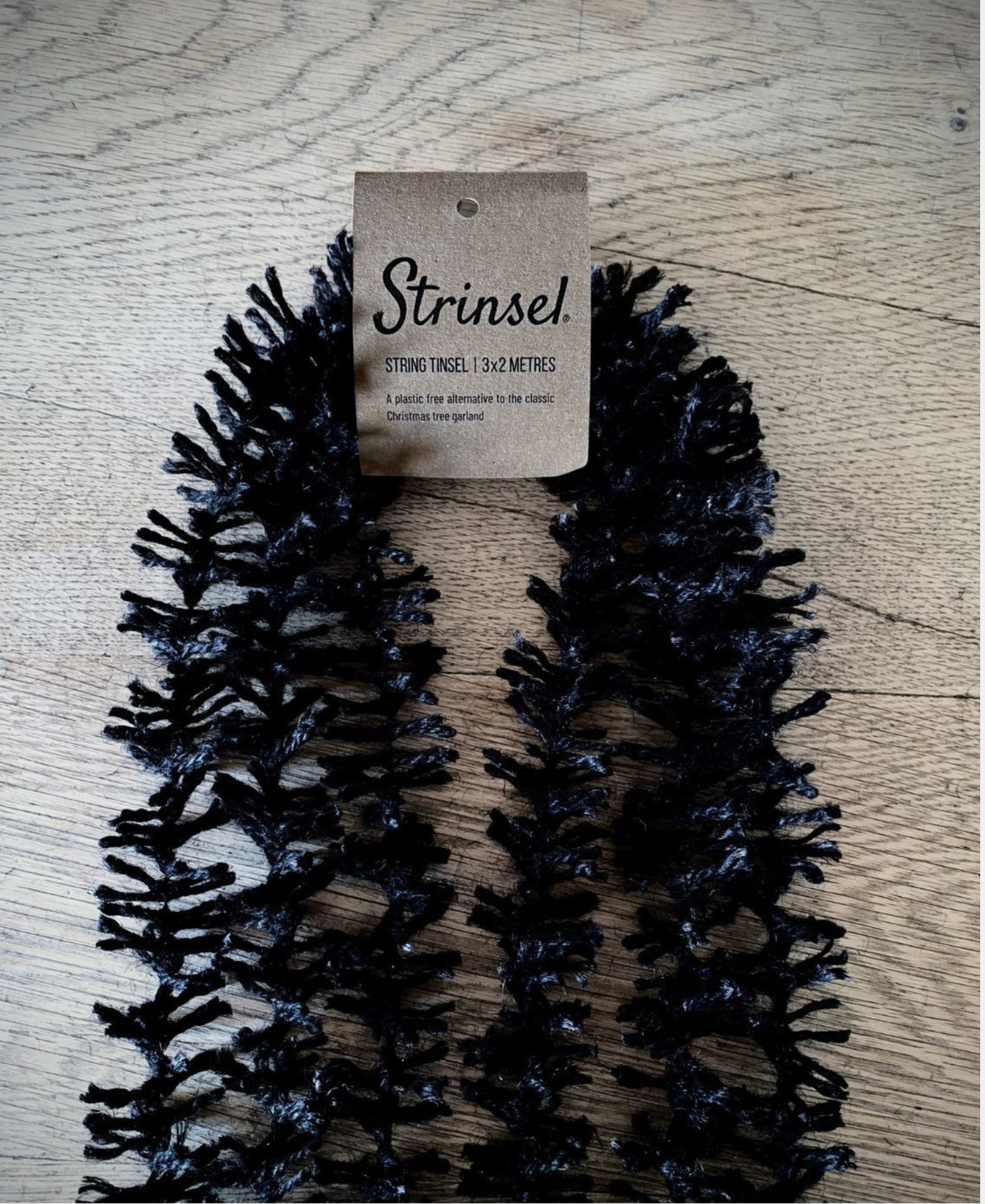 Multipack of black jute Spider leg Strinsel string tinsel garland with kraft label laid out on an oak table top