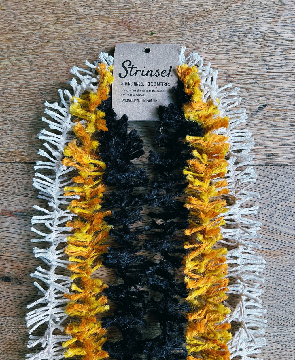 Strinsel string tinsel in natural cotton, orange jute and black jute packaged with a kraft label laid out on an oak table
