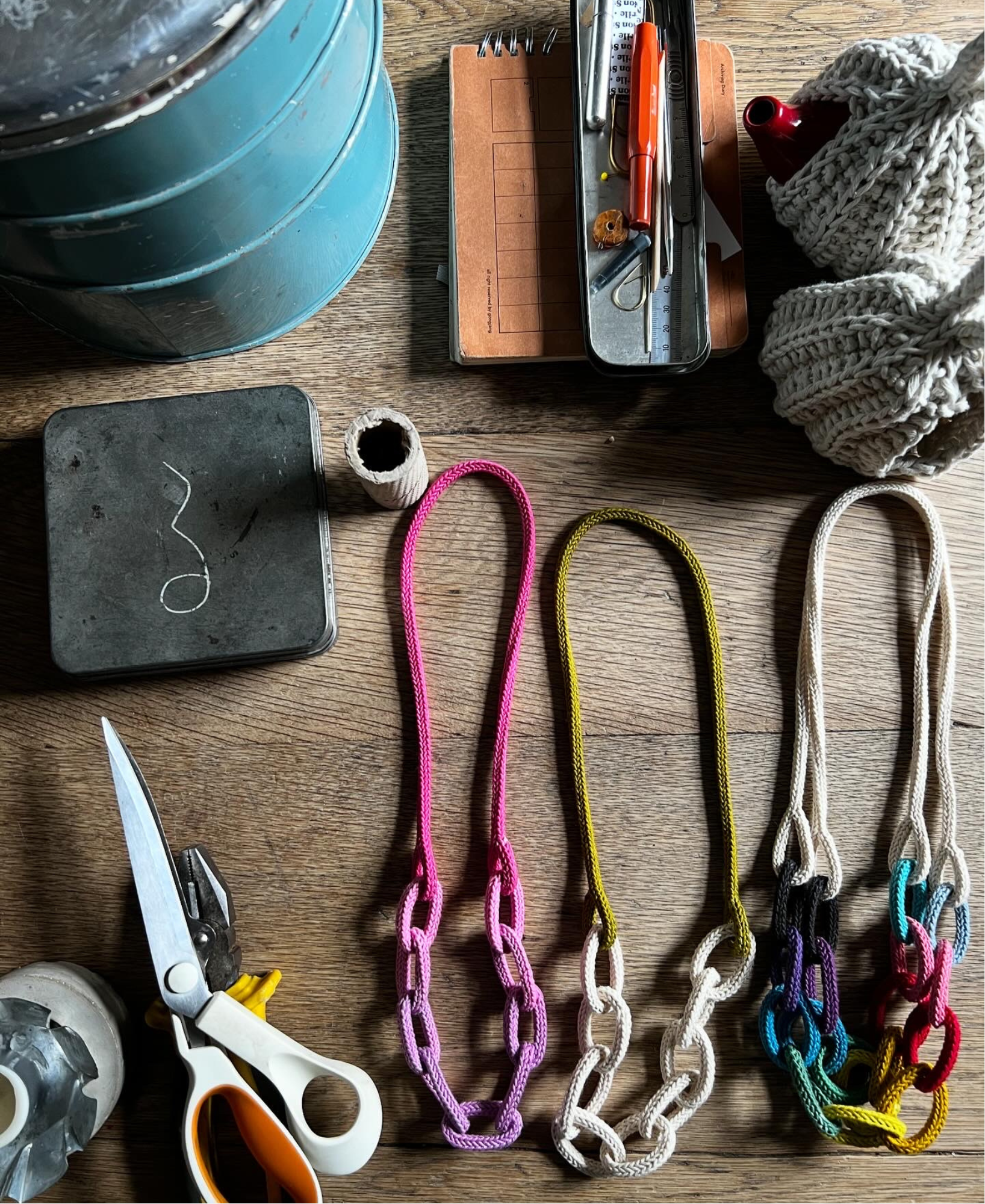 Colourful chunky chain knitted string necklaces and wooden table surrounded by tools and materials