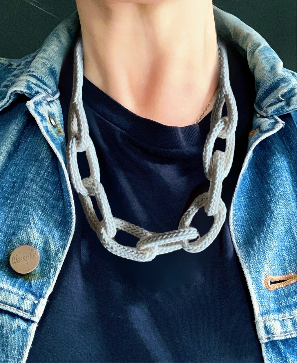 Person wearing a denim jacket and dark shirt with a chunky chain knitted string necklace