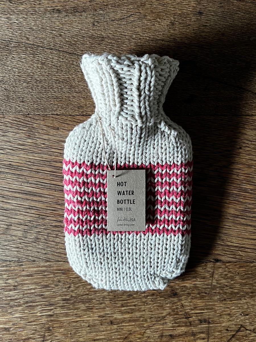 Knitted mini hot water bottle with a label on a wooden surface