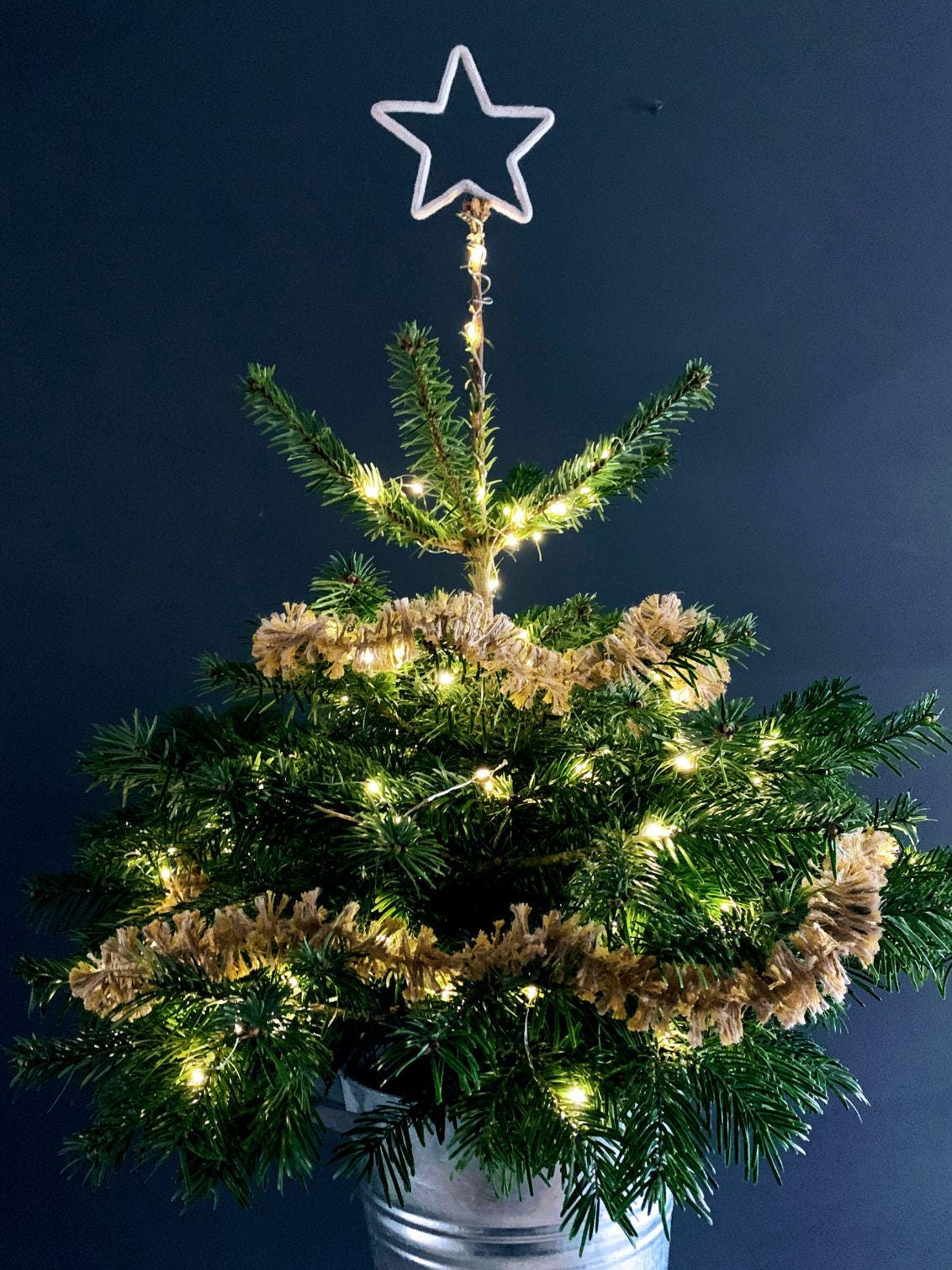 Small Christmas tree with a star topper and draped in jute Strinsel string tinsel against a dark blue background