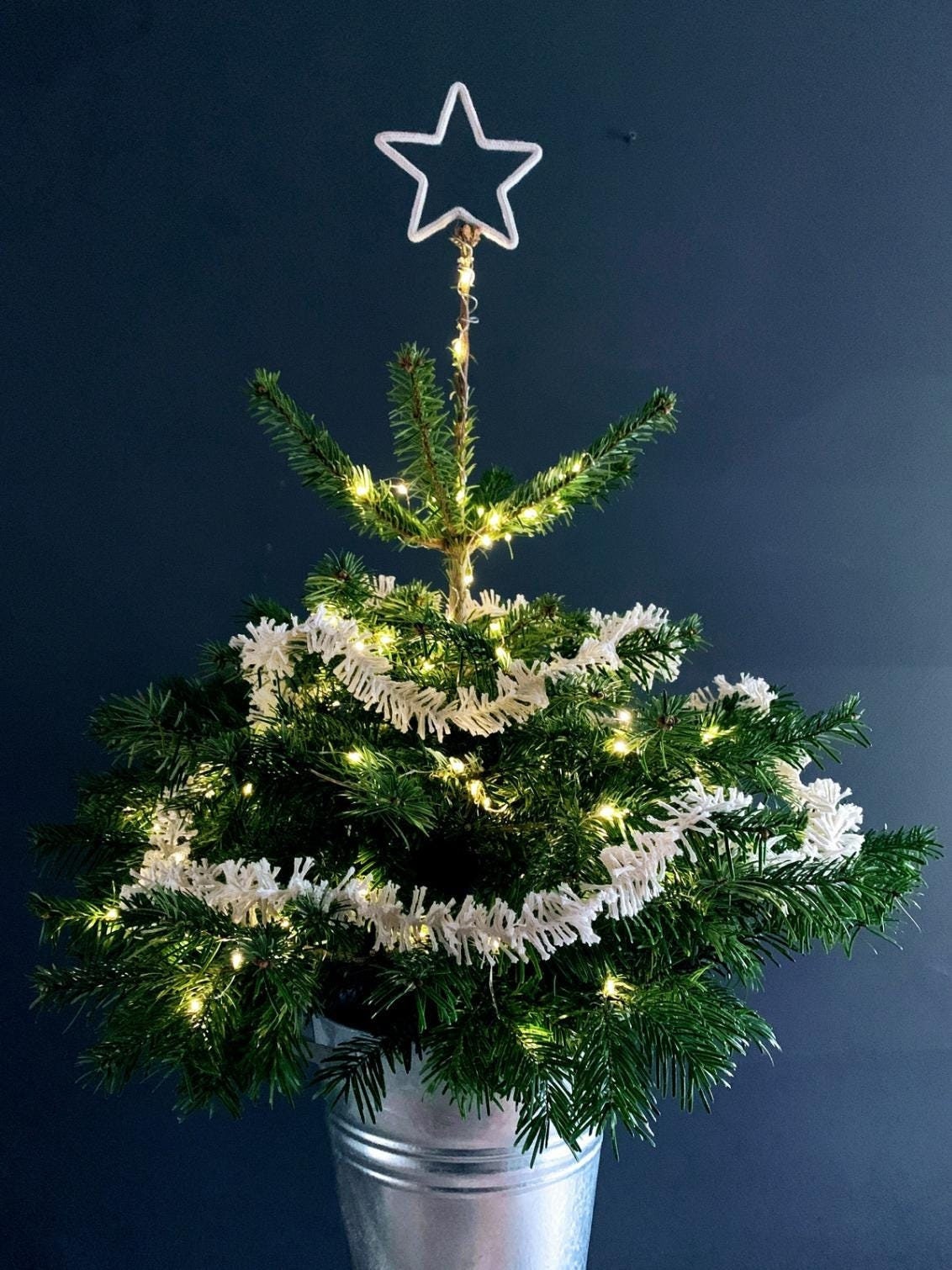 Small potted Christmas tree with lights and a star draped in Strinsel string tinsel on a dark background